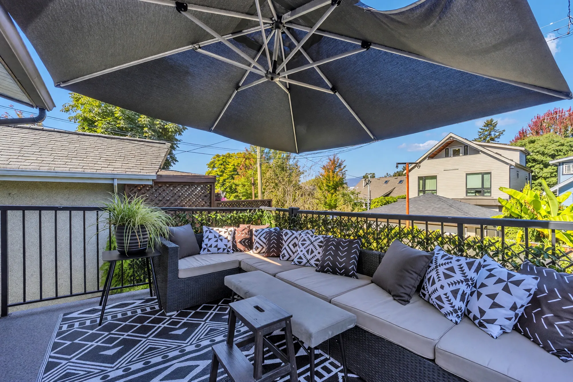 The balcony's sectional and cushions along the railing, the neighbours' roofs beyond
