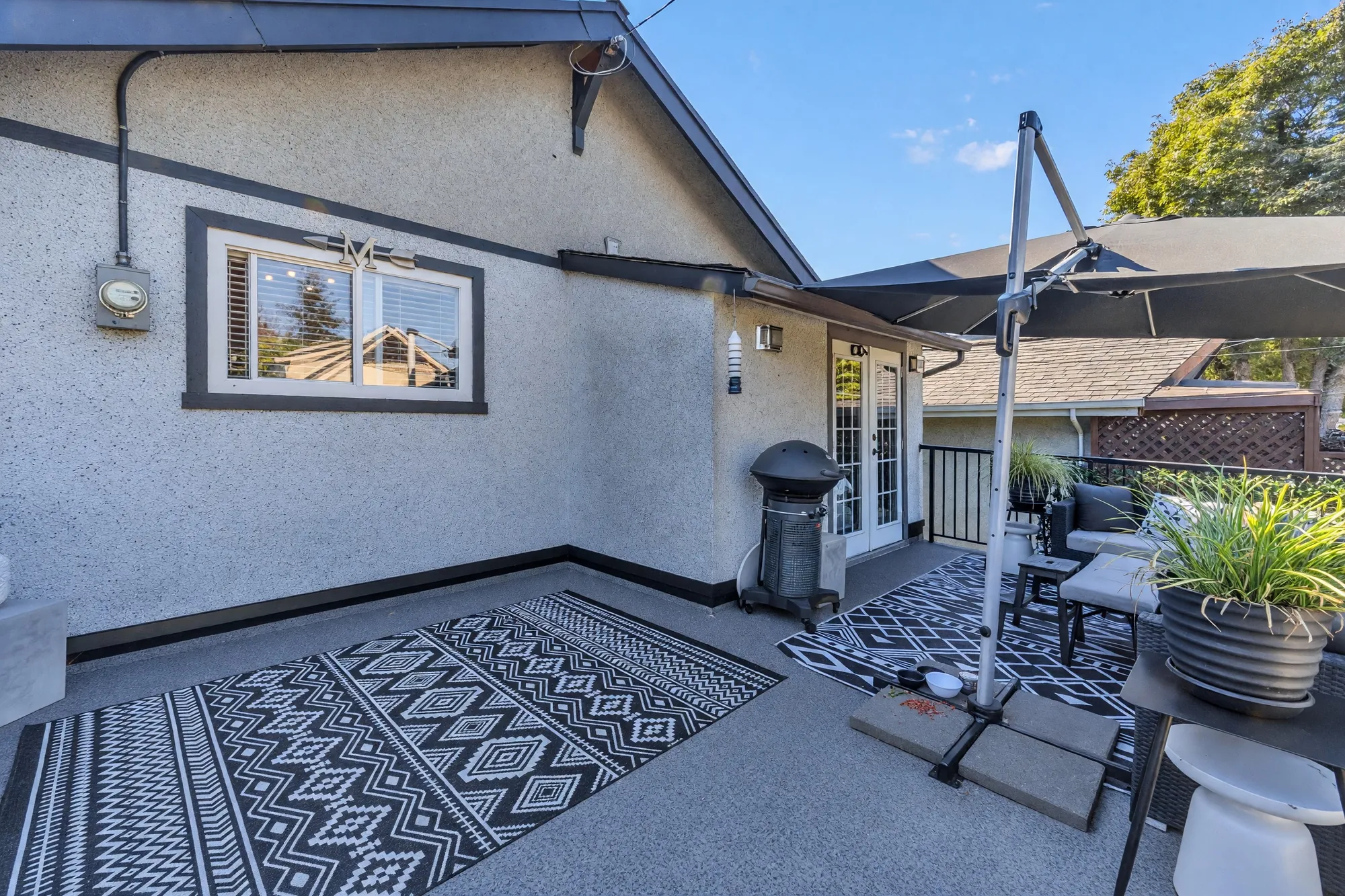 The balcony toward the house: the kitchen window, the umbrella, outdoor rugs on the deck, a planter