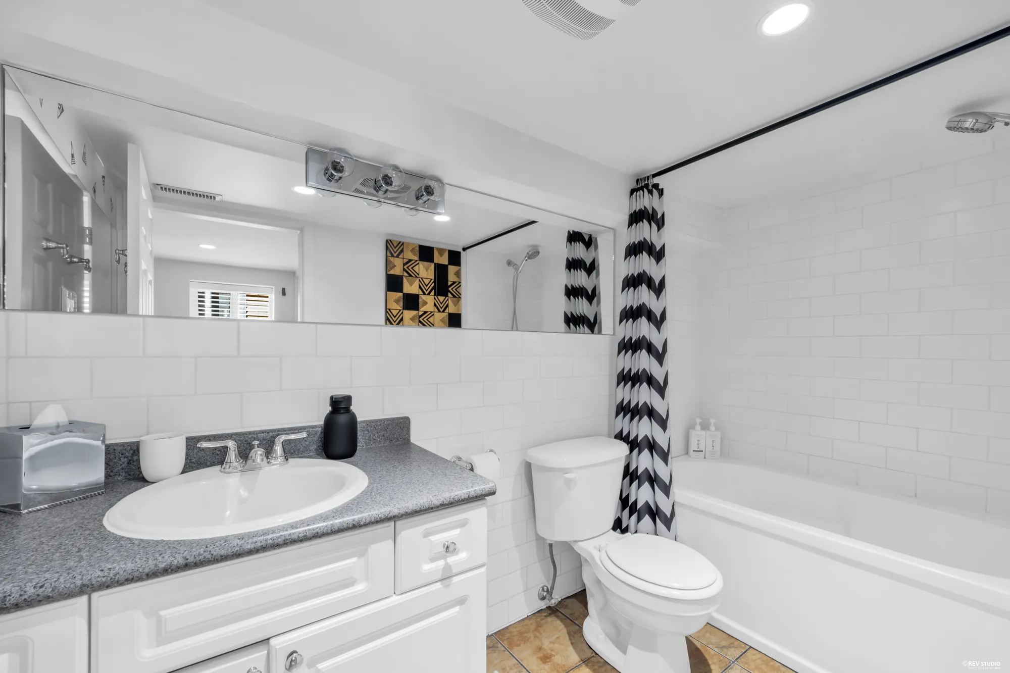 The lower bathroom: a white vanity with a grey counter, white subway tile, a tub with a striped shower curtain, tile floor