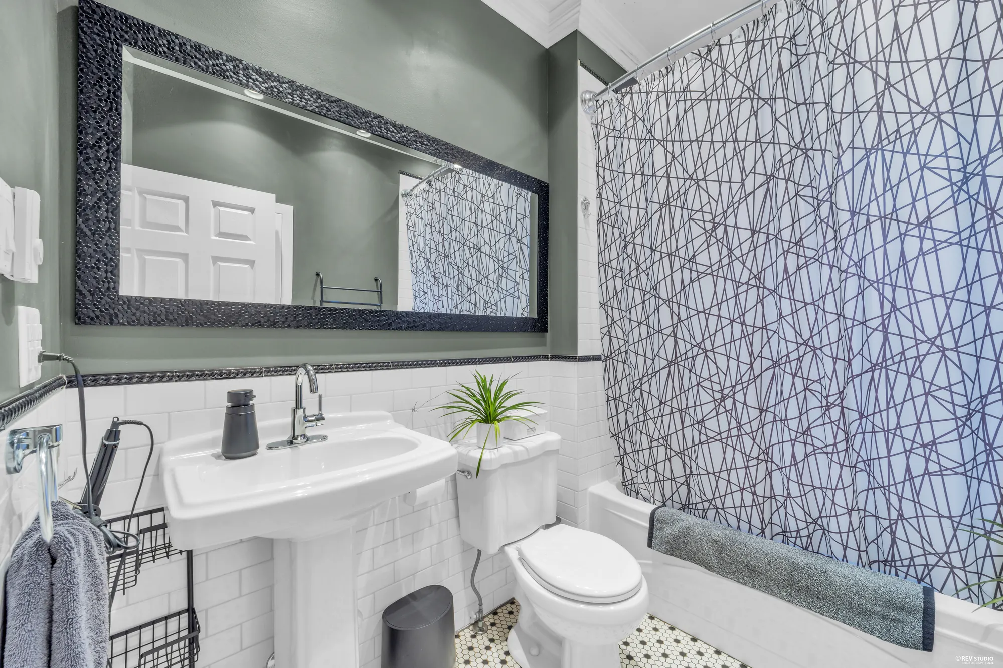 The main-floor bathroom: a pedestal sink, white subway tile with a black border, green walls, a hexagonal tile floor, a tub with a shower curtain