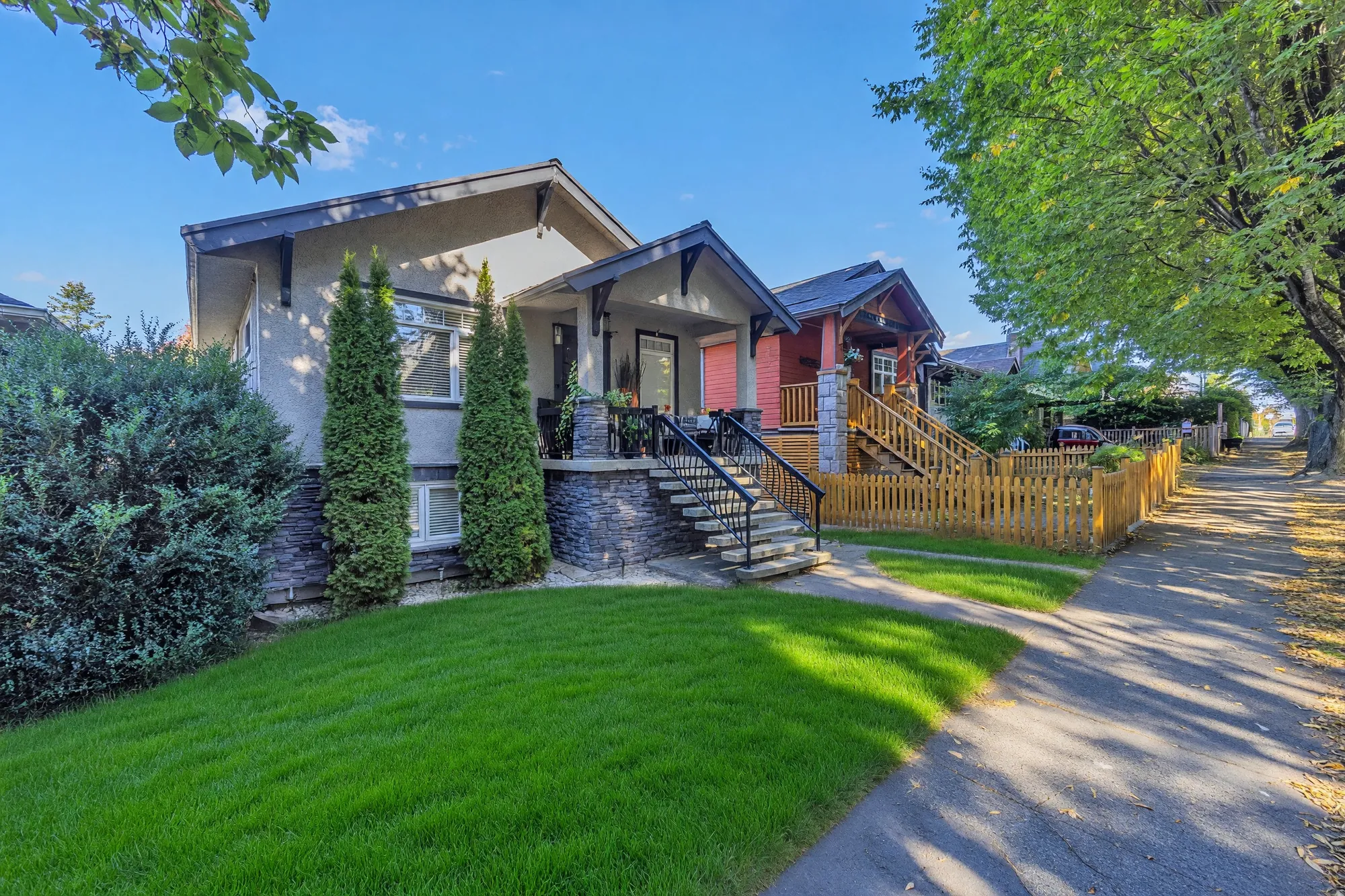 The front from the east under the street trees, the picket fence, the porch
