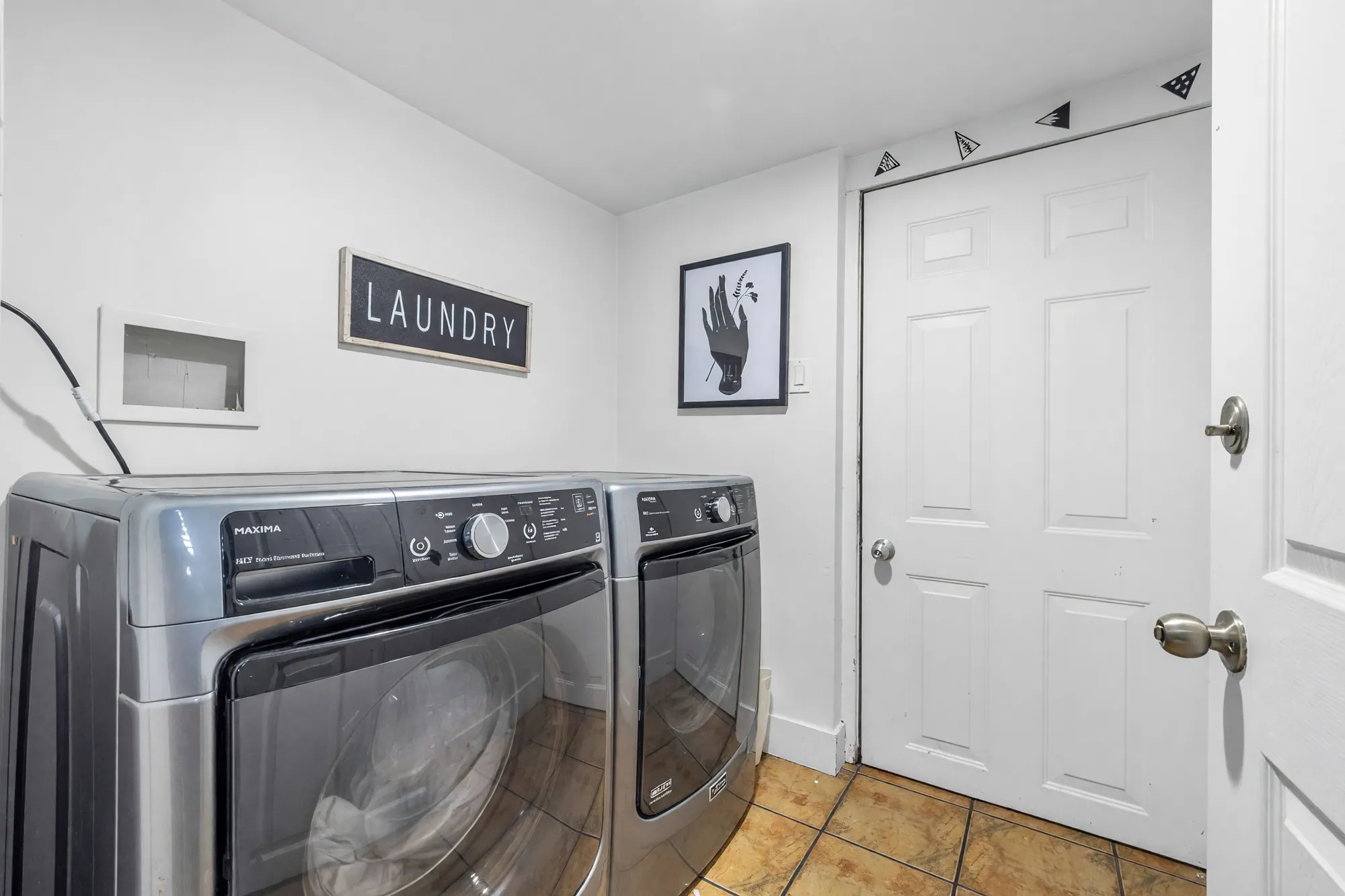 The laundry: a front-loading washer and dryer, a Laundry sign, a white door, tile floor