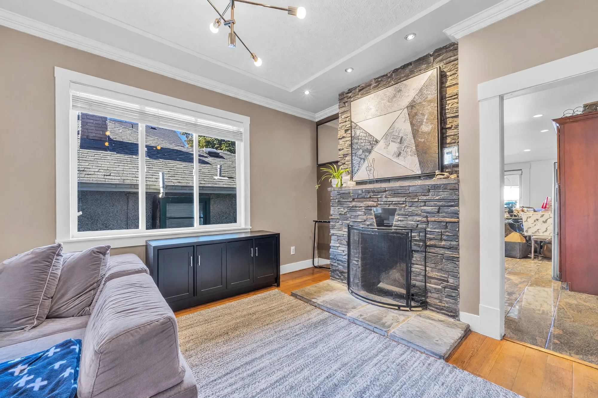 The dining end: a stacked-stone fireplace with a black insert, a picture above it, the side window with black cabinets below, the doorway to the kitchen