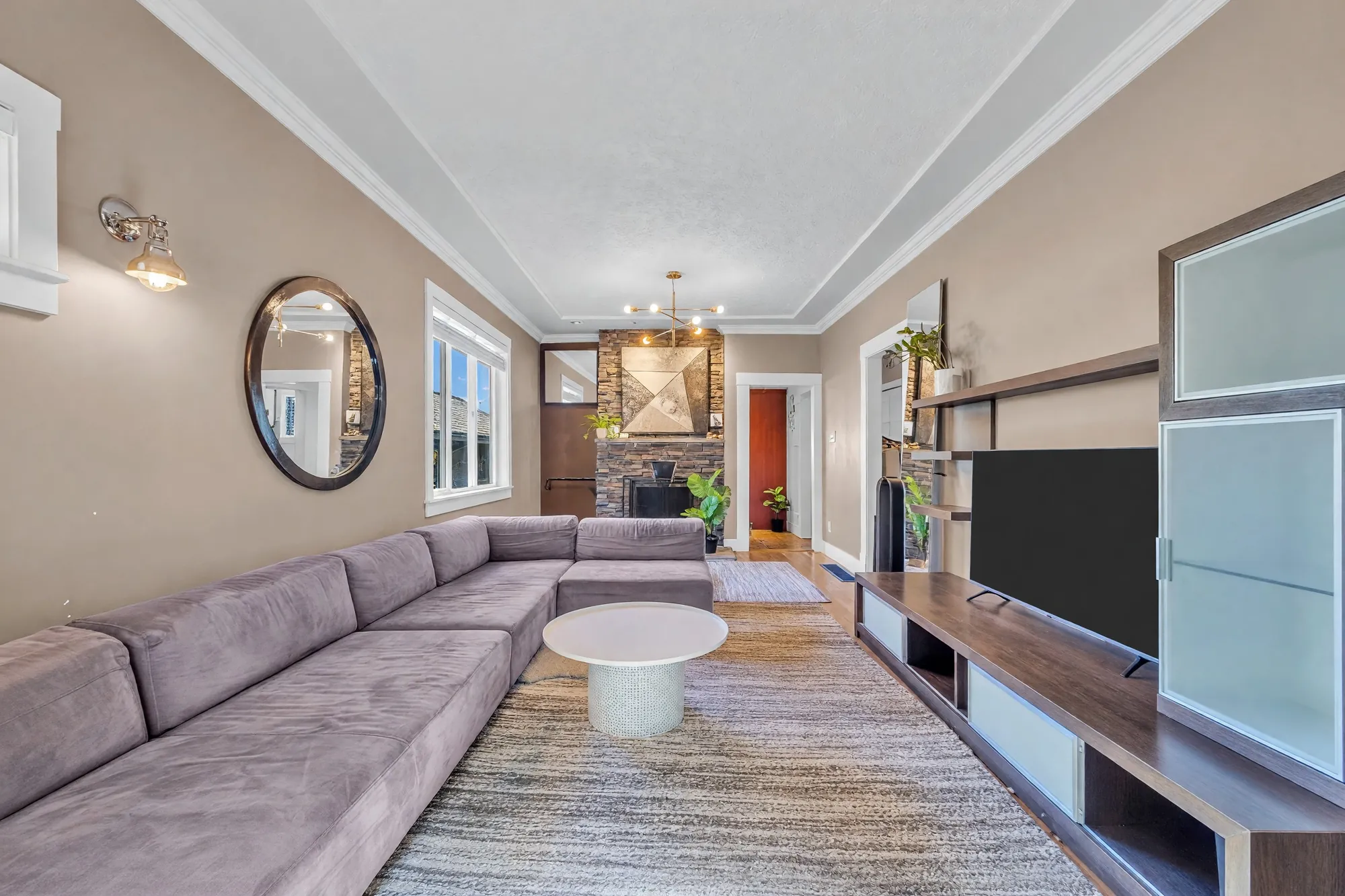 The room from the mirror wall: the sectional, the television unit with a glass cabinet, the fireplace beyond