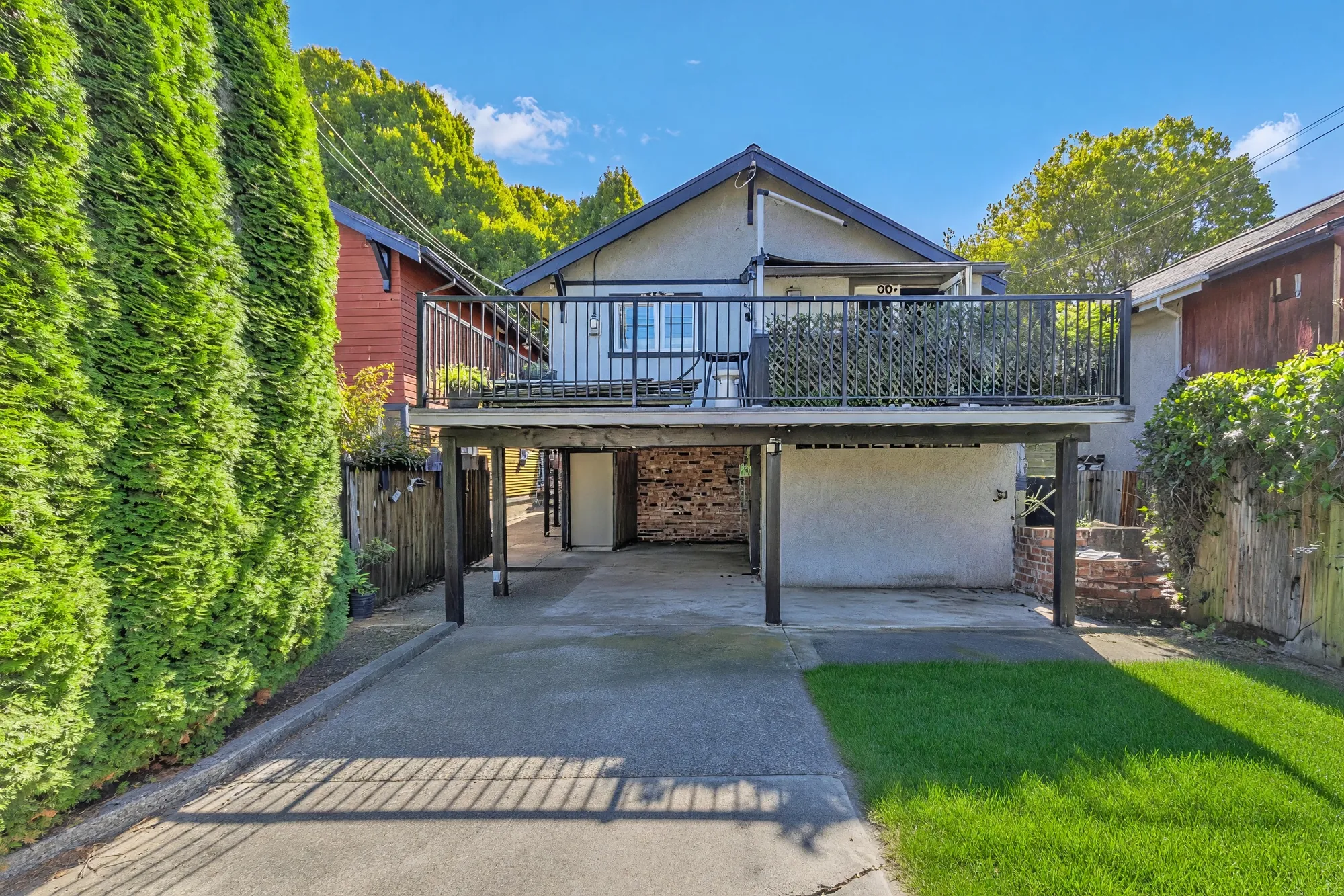 The back from the lawn side: the balcony, the parking bay, the hedge along the left, the neighbours' roofs beyond